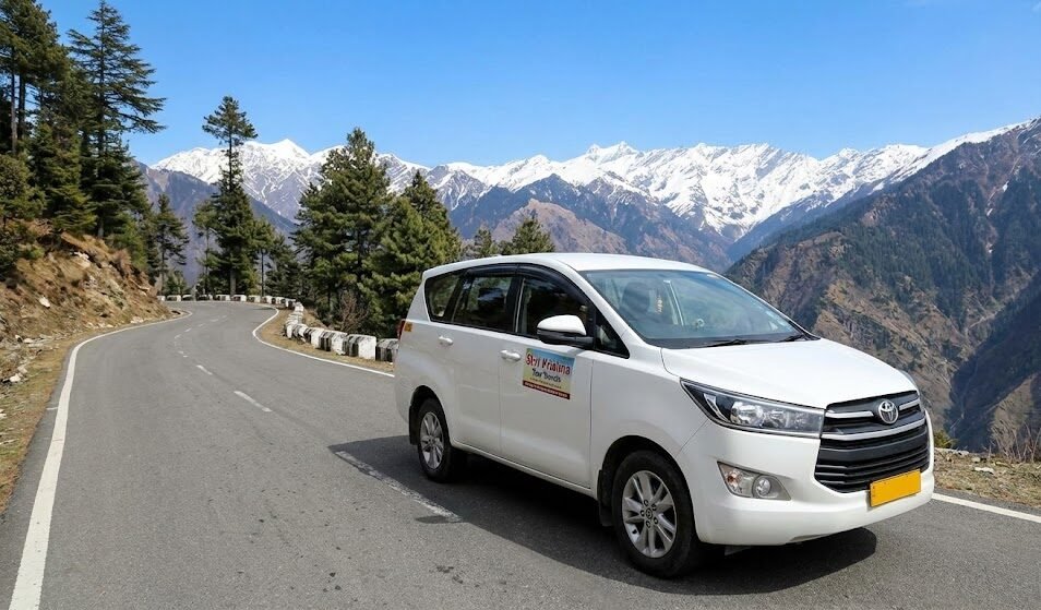 a white innova crysta taxi from shri krishna tour travels on a scenic mountain road during the chardham yatra with snow capped peaks in the background.