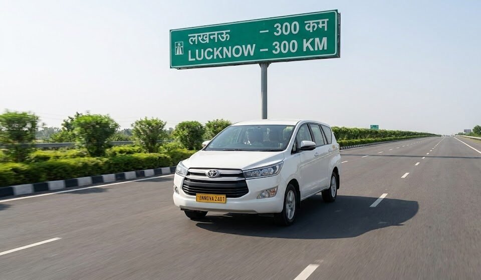 the same white toyota innova crysta taxi is driving on the smooth, multi lane agra lucknow expressway during the day. a large green overhead sign indicates lucknow 300 km